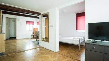 Una stanza con pavimento in legno, un letto, una televisione e una scrivania con cassetti.