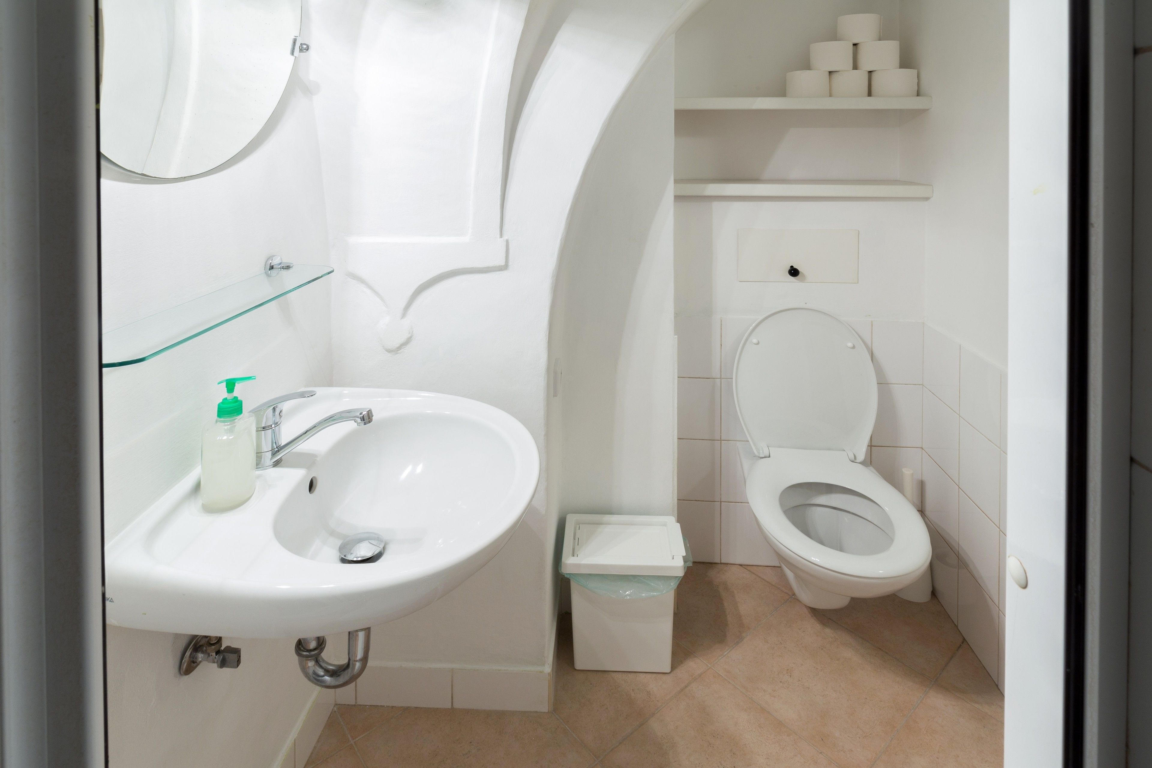 A bathroom with a white sink, mirror, toilet, and a trash bin.