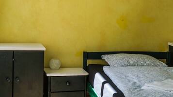 Quarto com cama, mesa de cabeceira, cômoda e luminária fixa na parede.