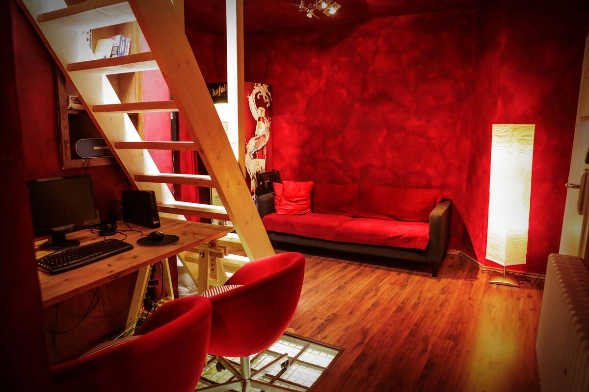 A room with a wooden desk, computer, red chair, red sofa, and a red wall.