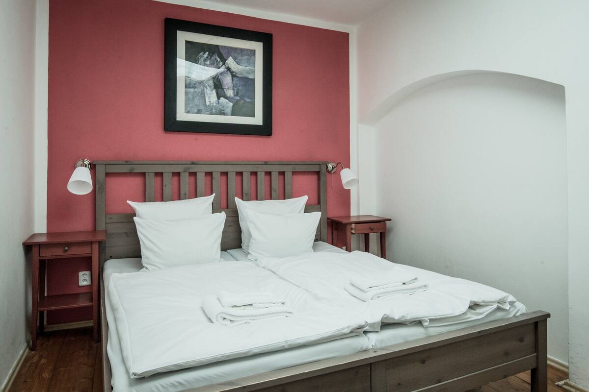 A neatly made bed with white linens, a wooden headboard, and a framed picture above it.