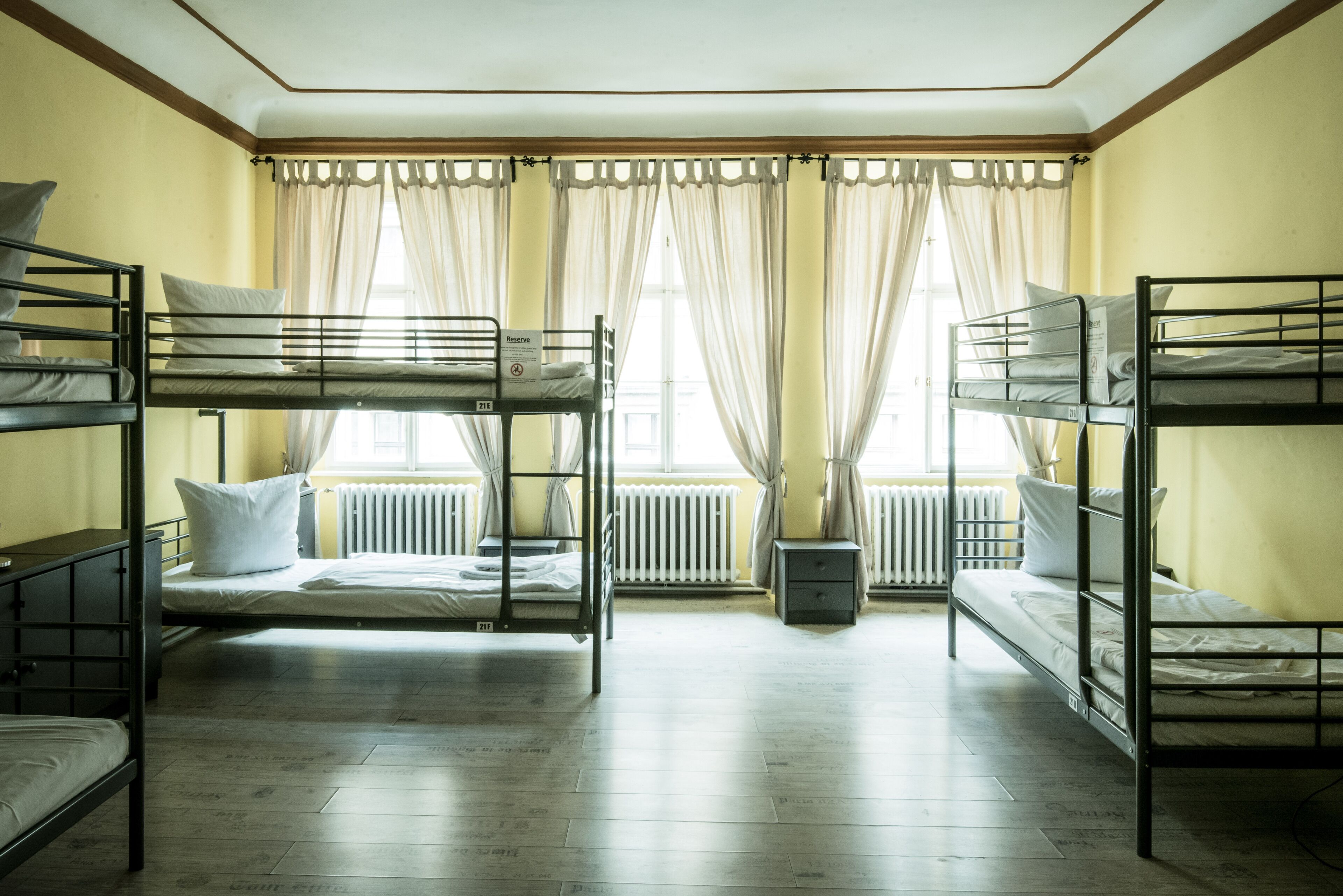 A dormitory room with bunk beds, a radiator, and a window with curtains.