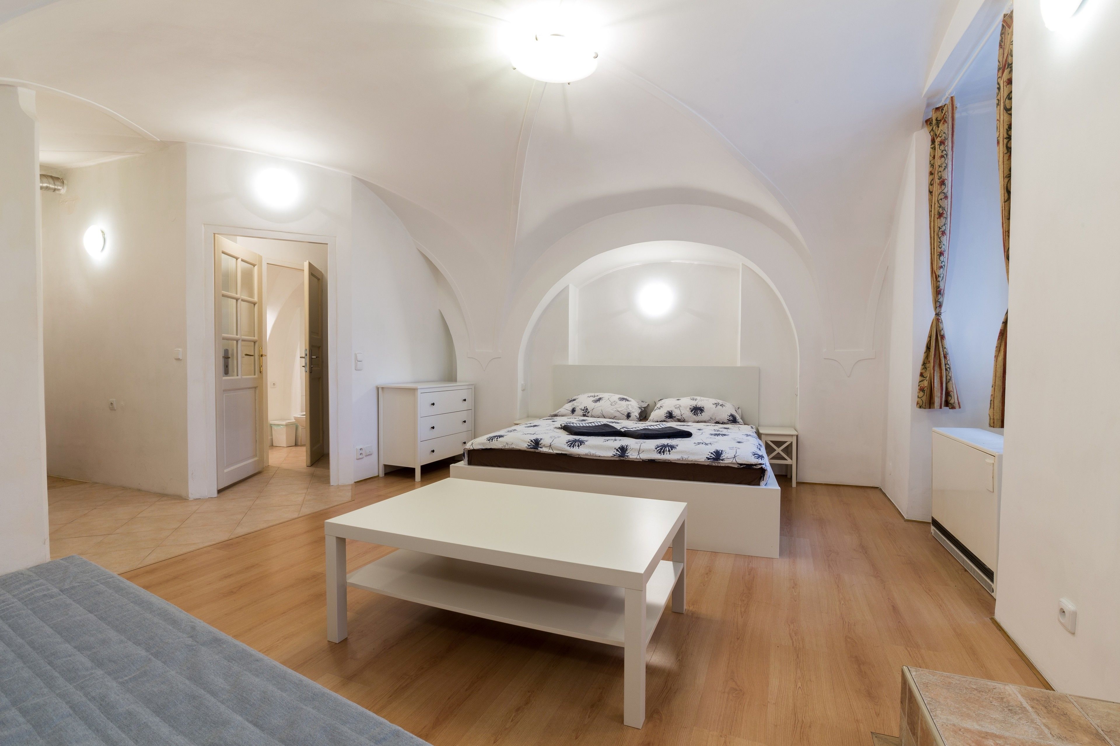 A bedroom with a bed, a bedside table, a wardrobe, and a door leading to another room.