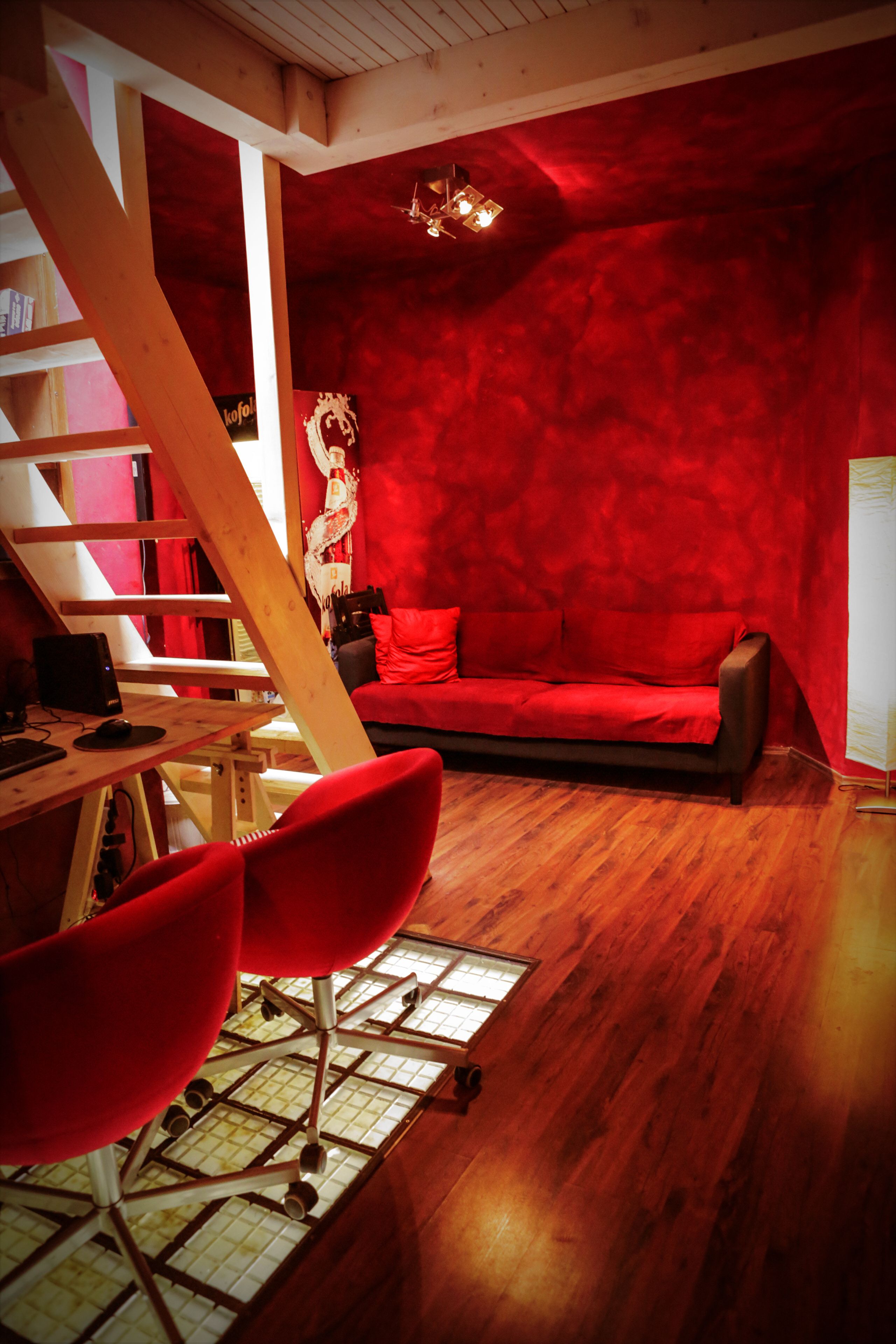 Quarto com parede vermelha, escrivaninha de madeira, sofá vermelho e cadeira vermelha.