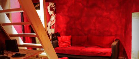 Quarto com parede vermelha, escrivaninha de madeira, sofá vermelho e cadeira vermelha.