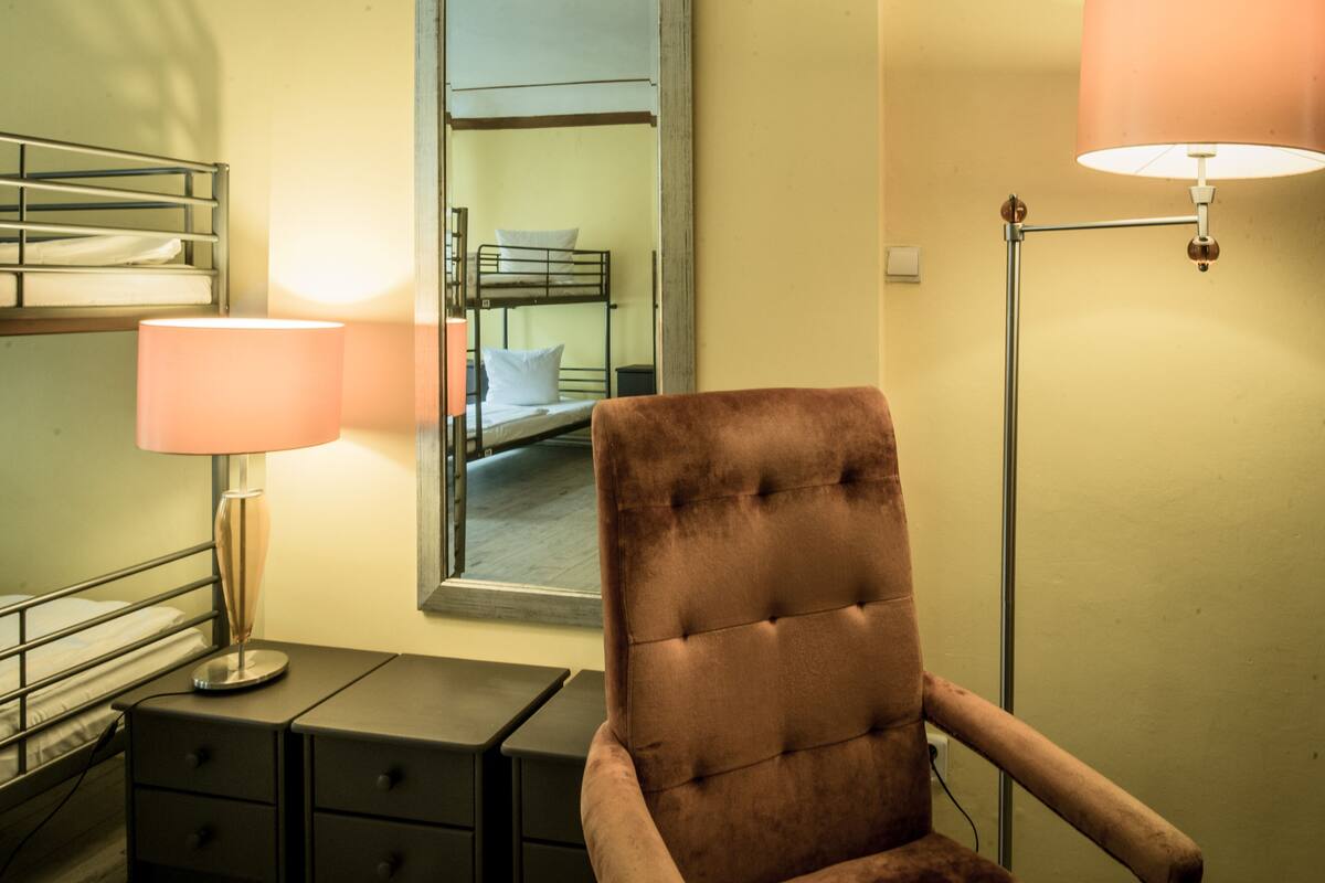A hotel room with a single bed, a chair, a bedside table, and a lamp.