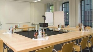 A conference room with long tables, chairs, a projector, and a whiteboard. - Hotel Lederfabrik (Muelheim an der Ruhr)