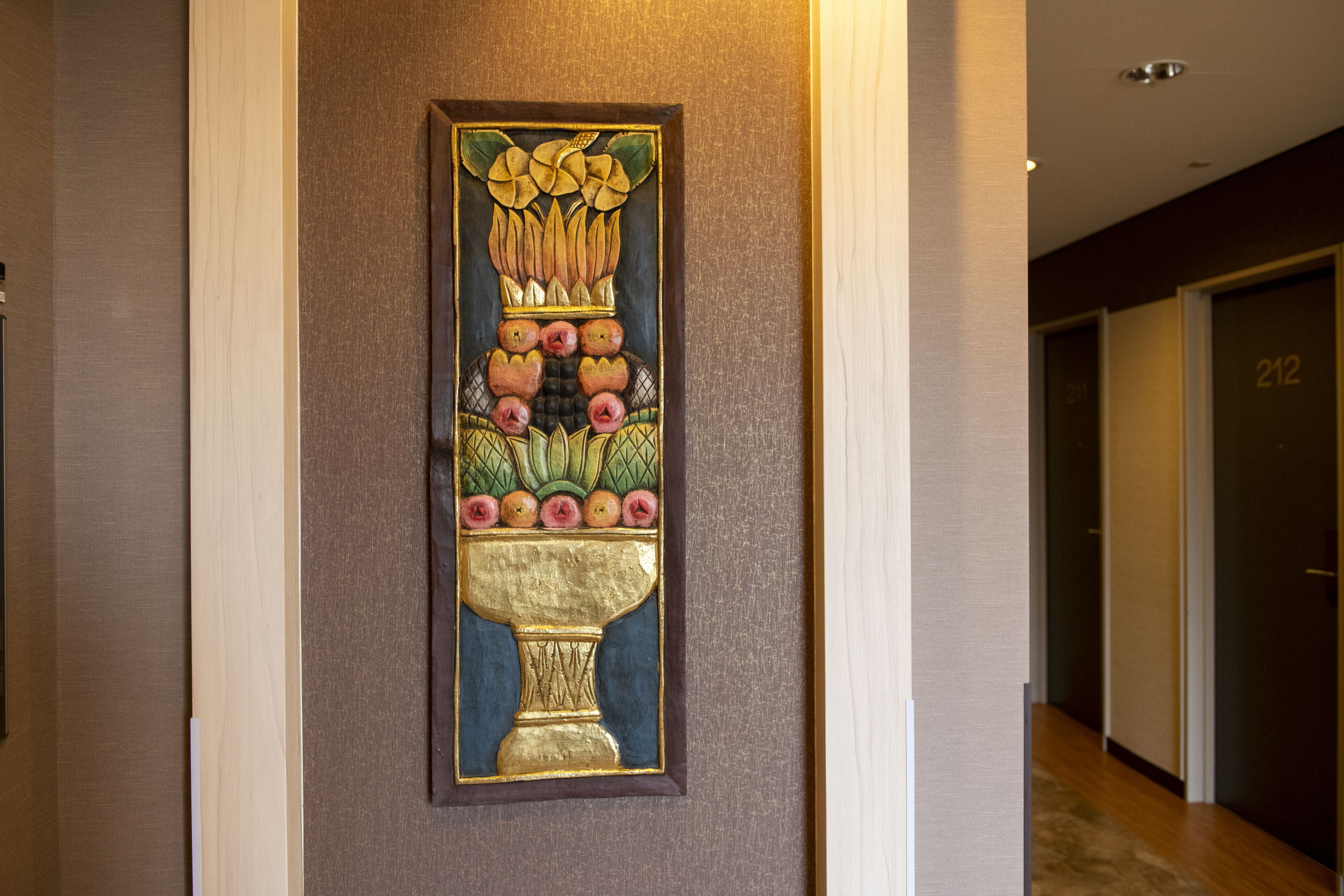 A hallway with a decorative wall art piece featuring a vase with fruits and leaves.