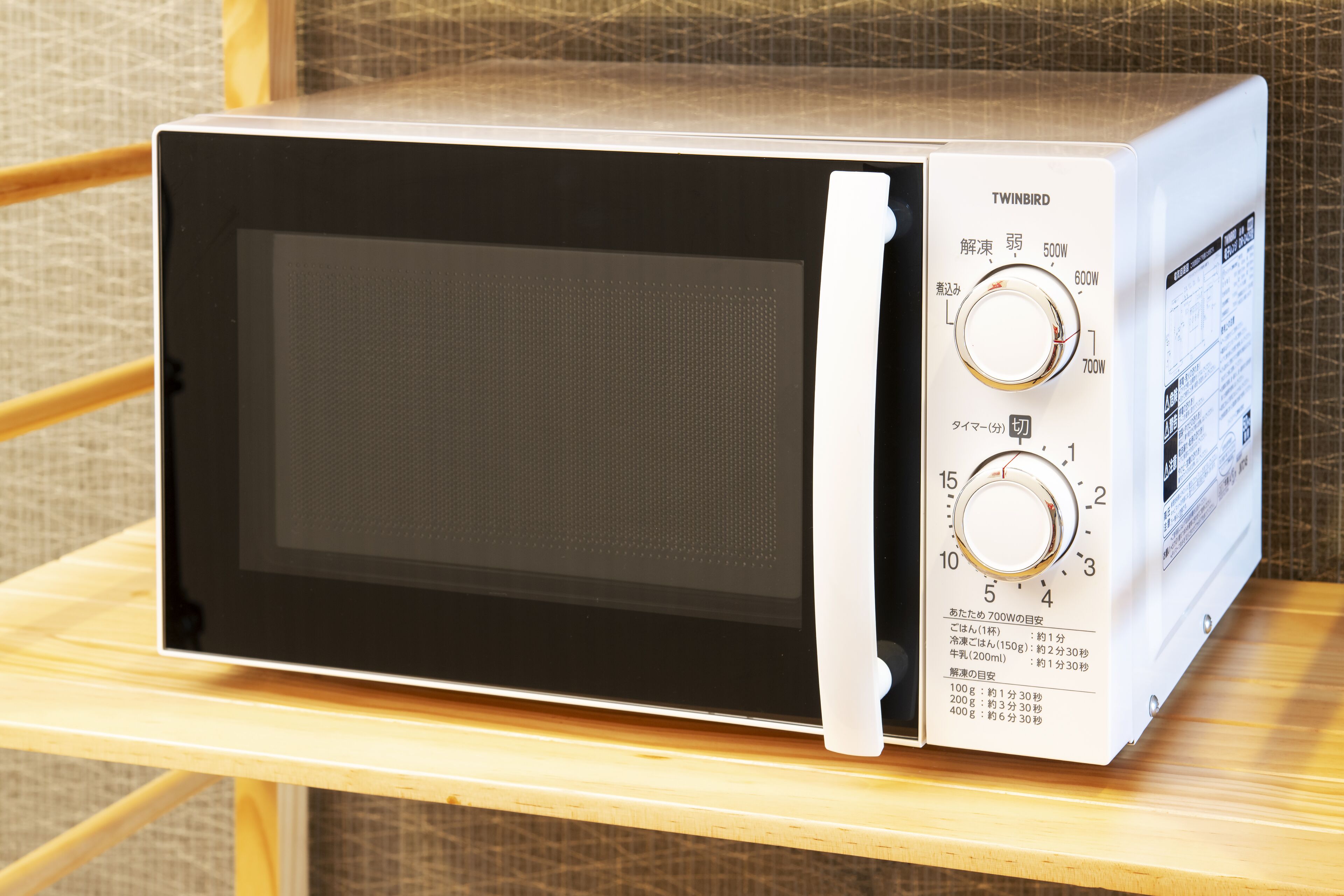 A microwave oven with two dials and a digital display, placed on a wooden shelf.