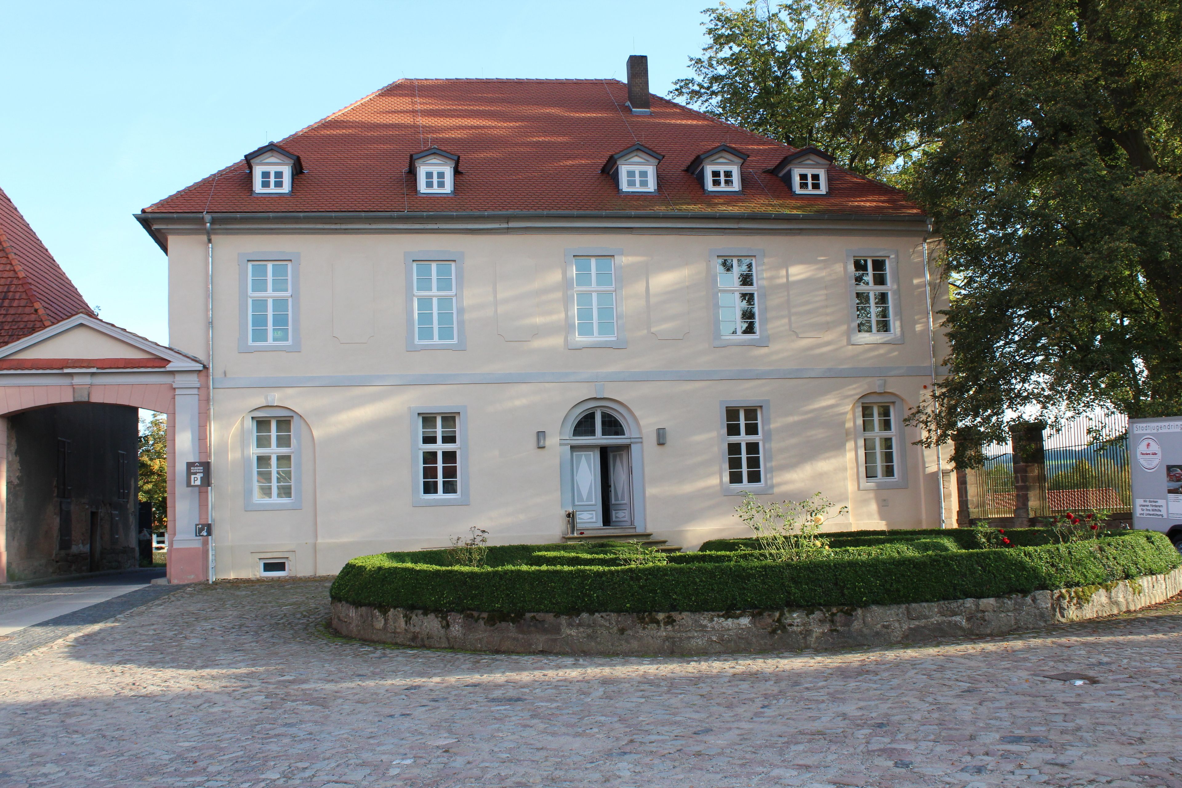 A two-story building with a red-tiled roof, multiple windows, and a small entrance door.