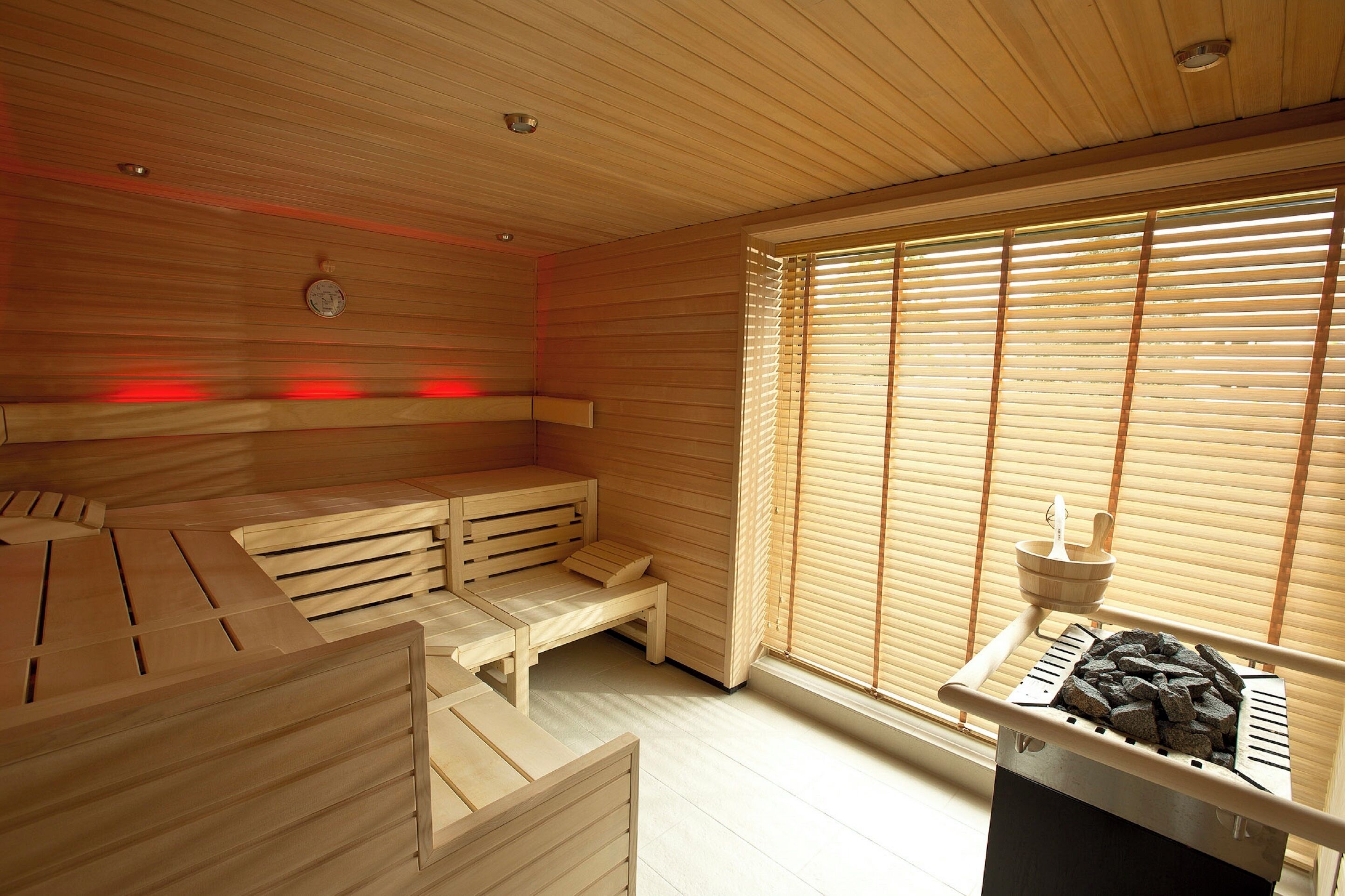 A sauna room with wooden benches, a bench with a footrest, and a heater with charcoal.