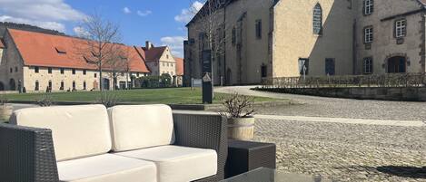 Un patio con mobiliario exterior, suelo de piedra y edificios históricos al fondo.