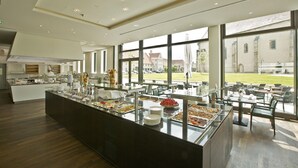 Een moderne eetruimte met een buffetopstelling, grote ramen en uitzicht op het exterieur van het gebouw.