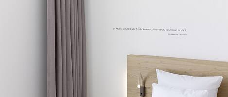 Ein ordentlich bezogenes Bett mit weißen Leinen und einem hölzernen Kopfteil. Eine Wandleuchte und ein Lichtschalter befinden sich darüber.