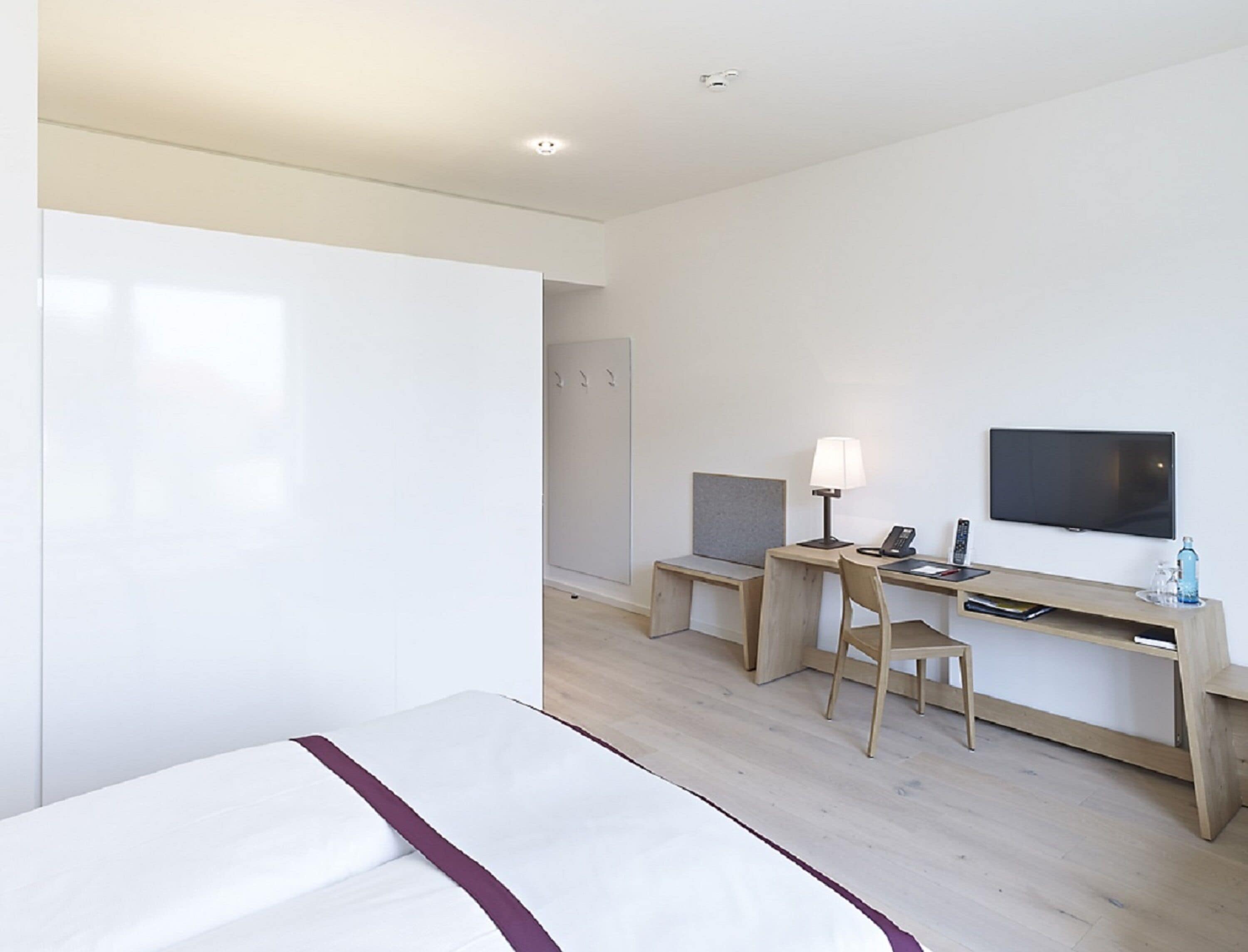 Een hotelkamer met een bed, een bureau met stoel, een televisie en een kledingkast.