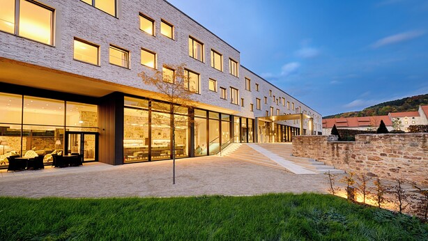 Een modern gebouw met een glazen gevel, zitplaatsen buiten en een stenen muur.