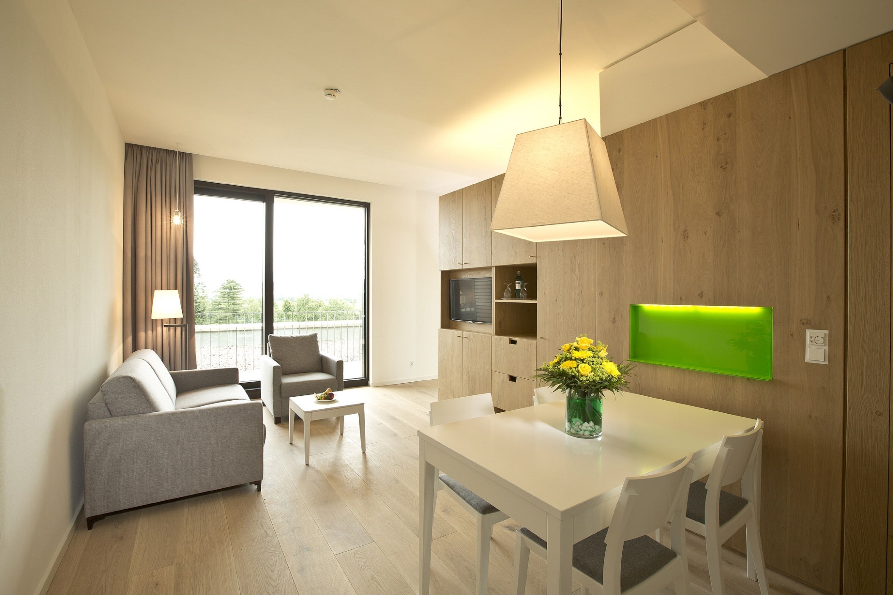 A modern living room with a sofa, a dining table, and a TV mounted on the wall.