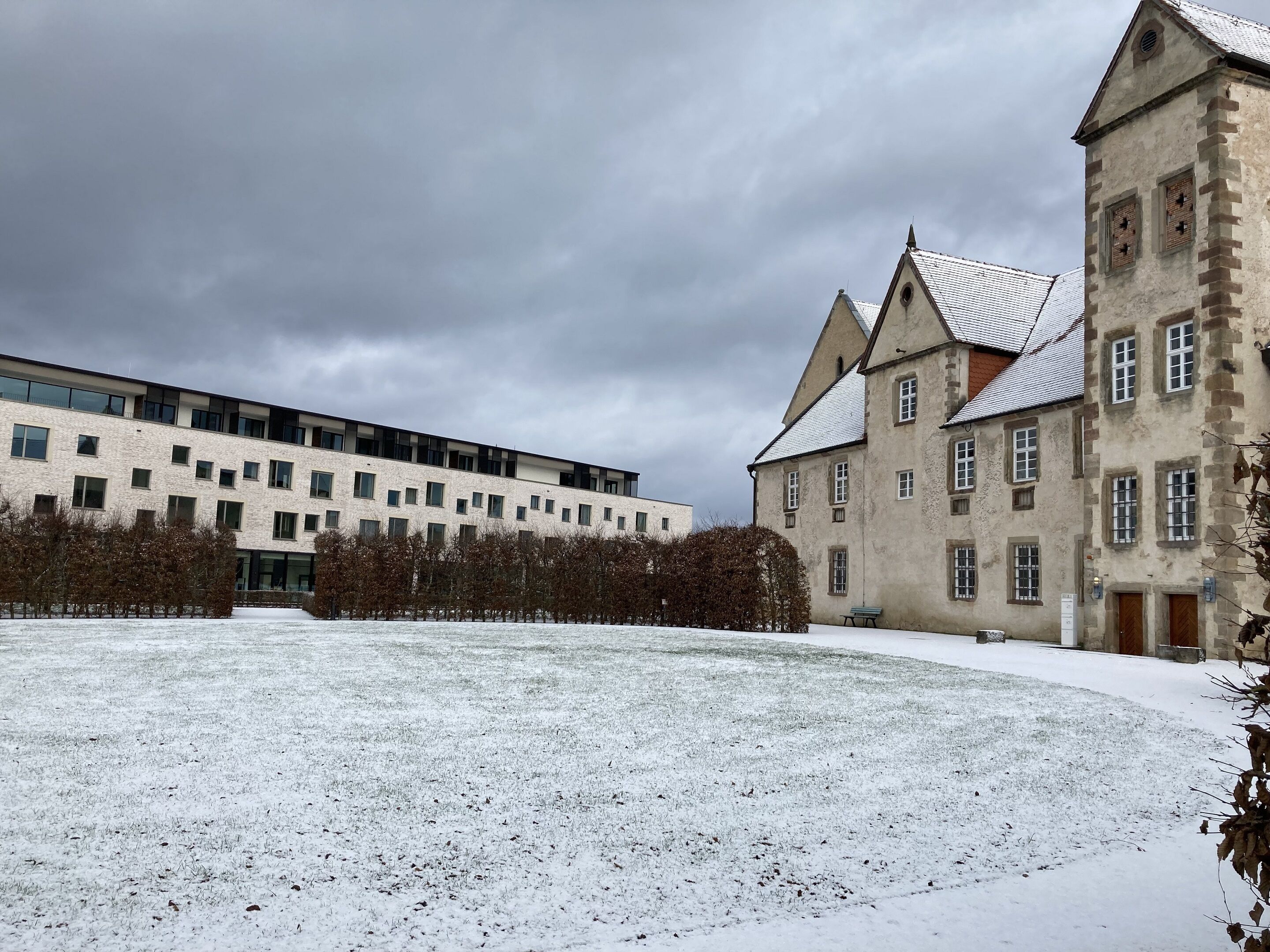 Un patio cubierto de nieve con un edificio moderno y otro histórico con una torre.