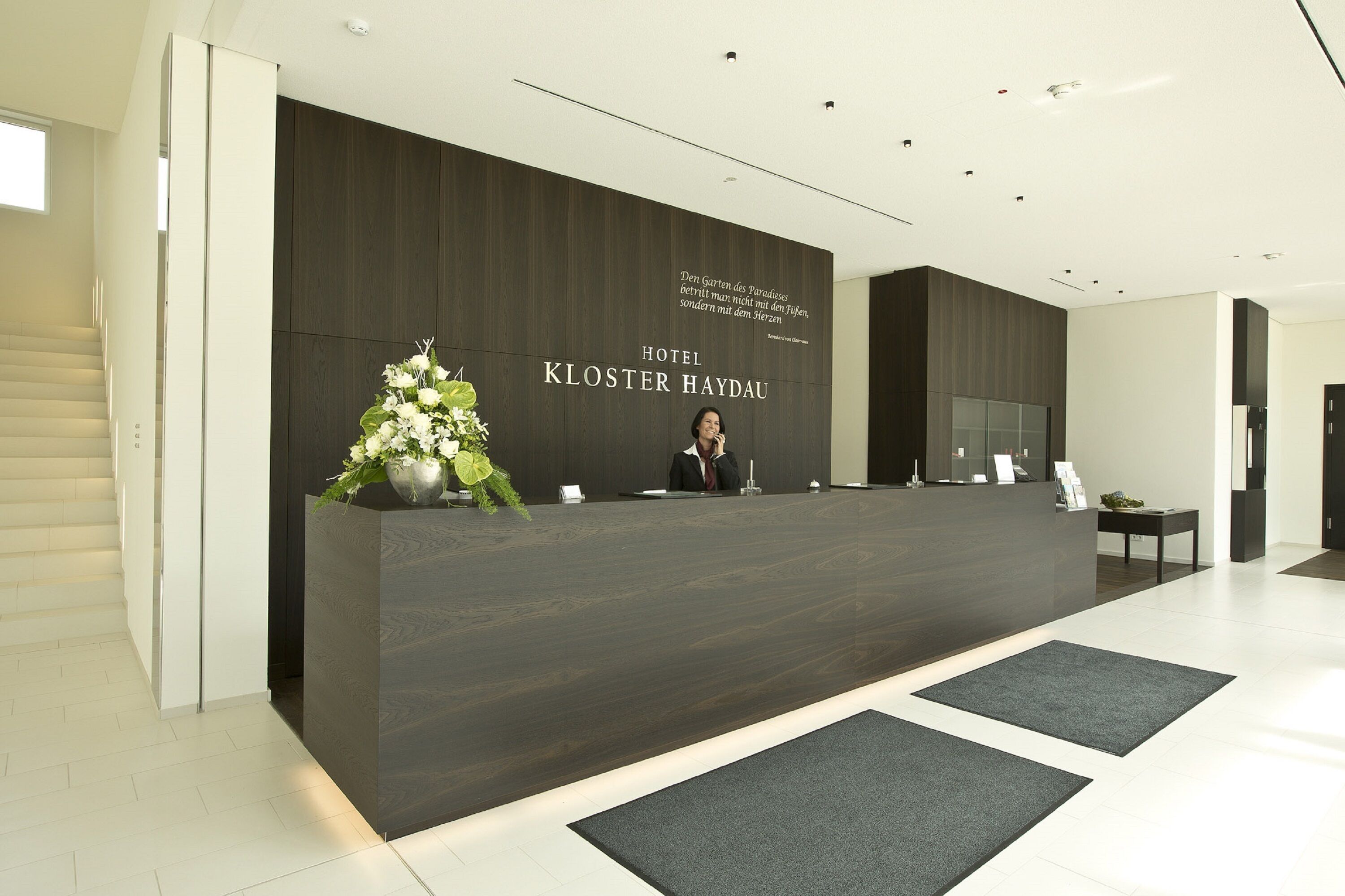Mostrador de recepción en el Hotel Kloster Haydau con un diseño moderno, una planta grande y un cartel sobre el mostrador.