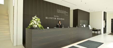 Mostrador de recepción en el Hotel Kloster Haydau con un diseño moderno, una planta grande y un cartel sobre el mostrador.
