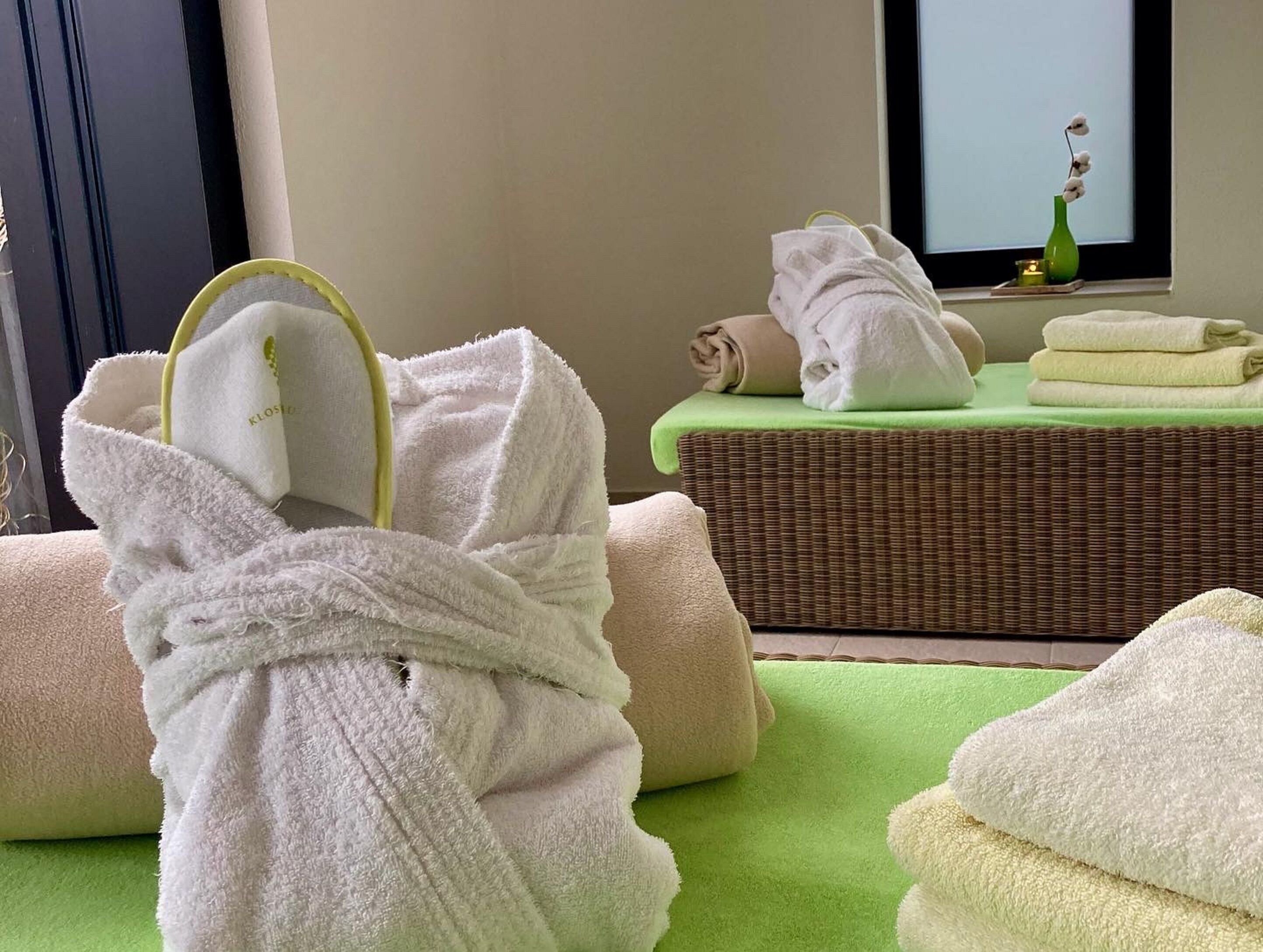 Habitación de spa con camilla de masaje, toallas y una esterilla verde.