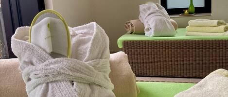 Habitación de spa con camilla de masaje, toallas y una esterilla verde.