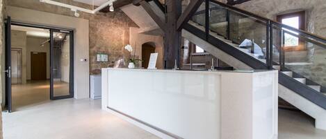 A modern interior with a reception desk, a staircase, and stone walls.