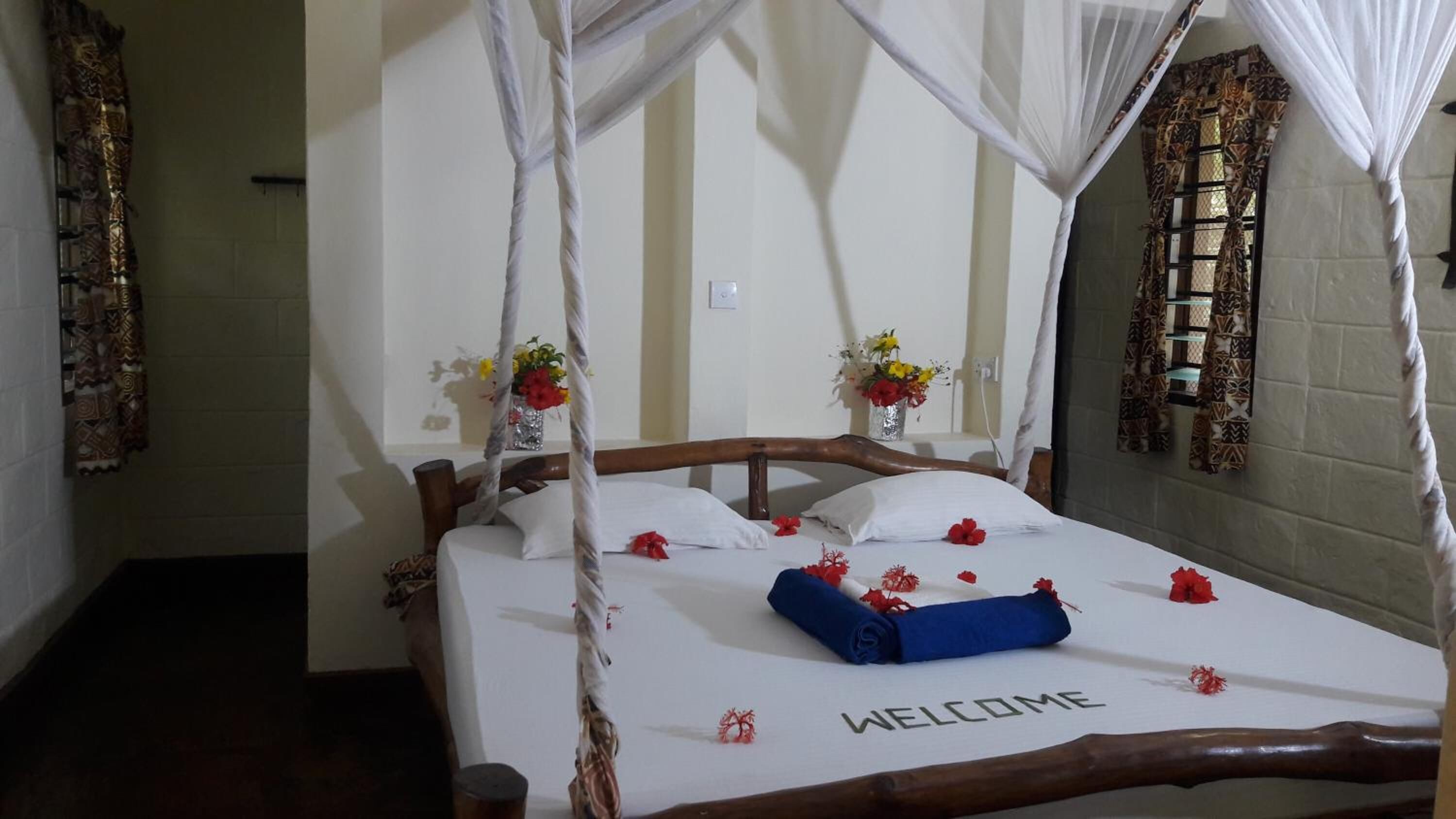 A bed with a canopy, a welcome mat, and two vases with flowers.