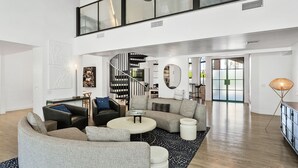 Een ruime woonruimte met een gebogen modulaire bank, een ronde salontafel en een zwart spiraaltrap naar een hoger niveau.
