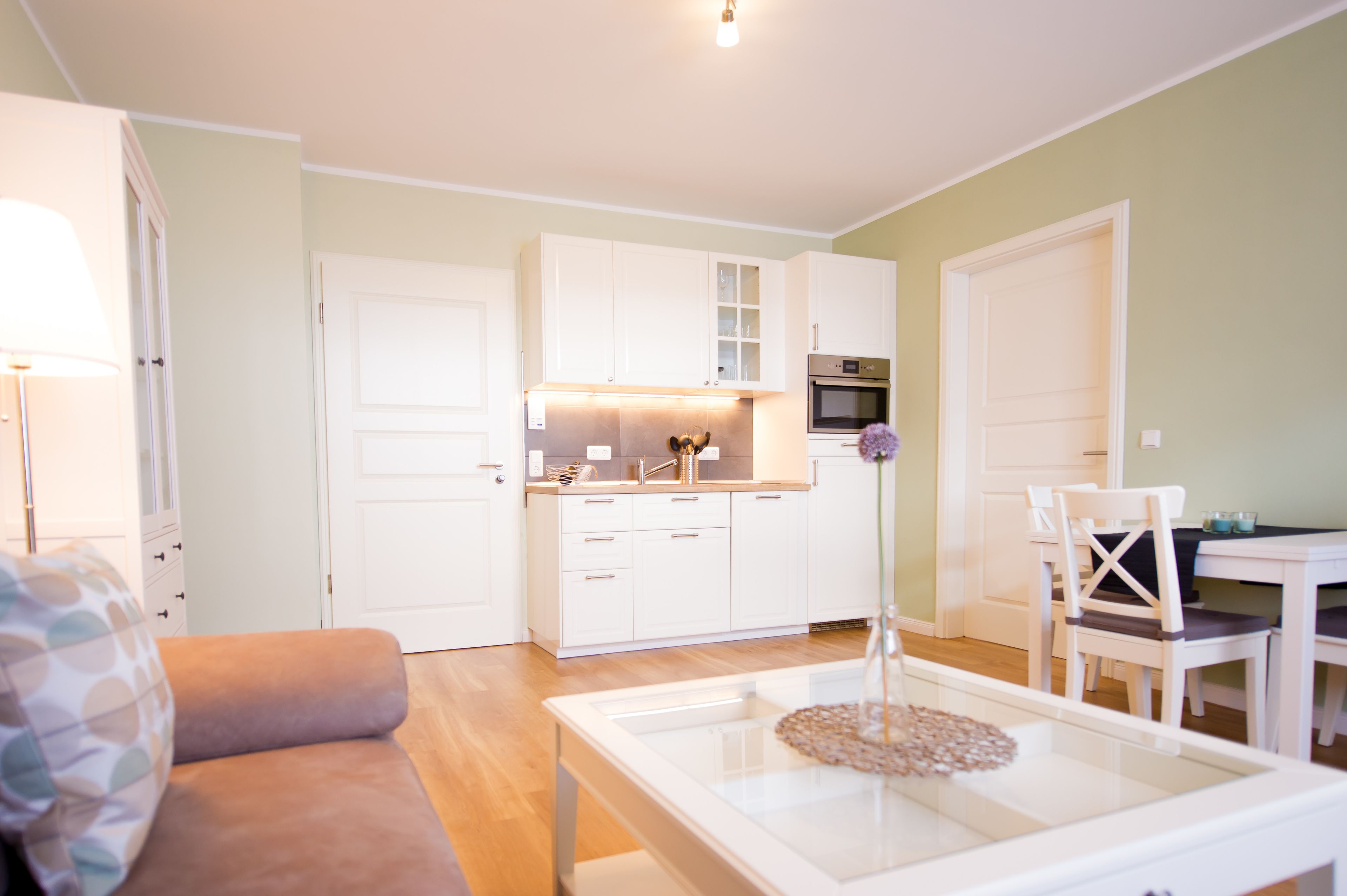 A modern kitchen with white cabinets, a dining table, and a sofa.