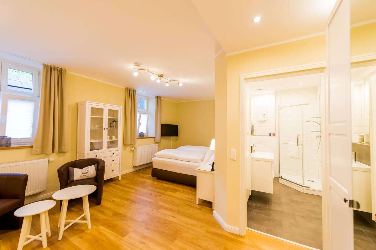 A modern hotel room with a bed, bedside table, and a small seating area with two stools.
