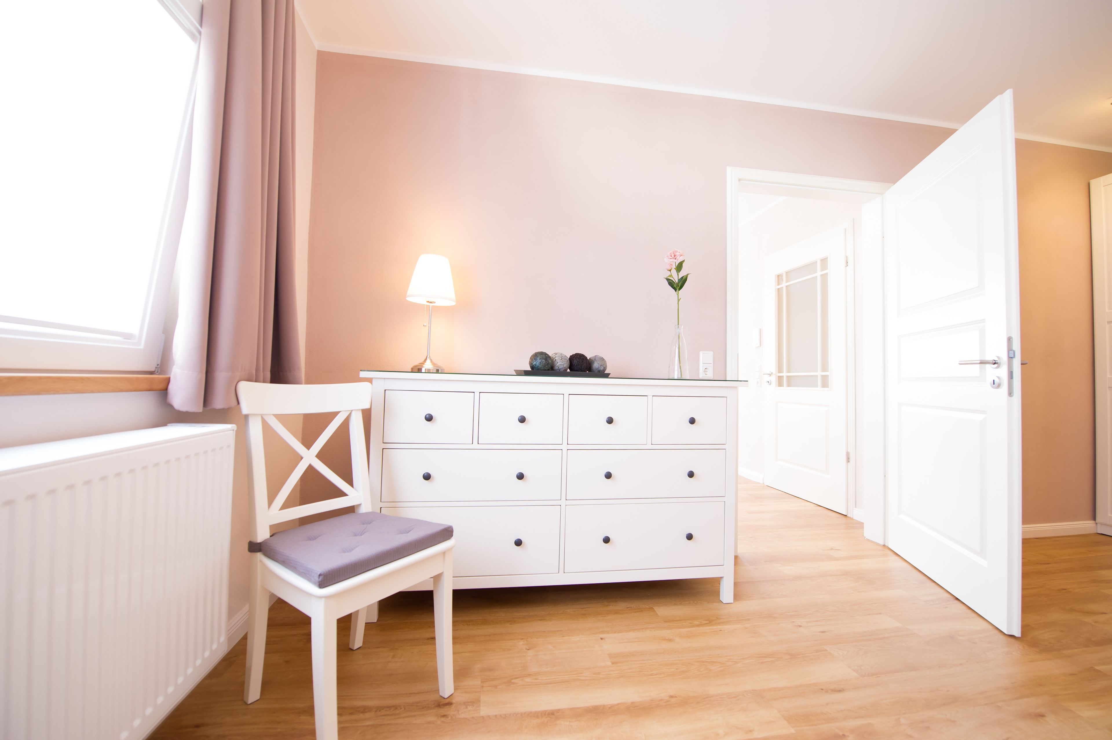 Une pièce avec une commode blanche, une chaise, une lampe et une porte.