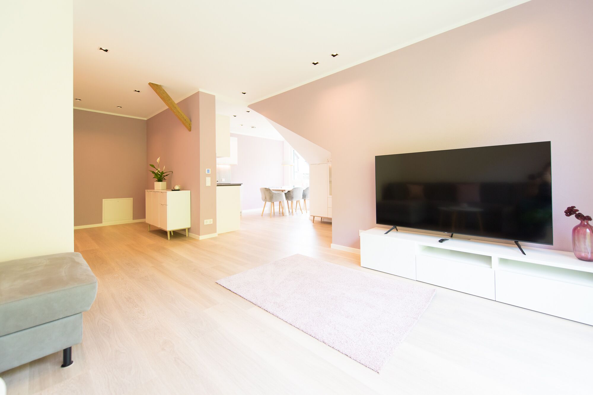 A modern living room with a flat-screen TV, a sofa, and a dining area in the background.