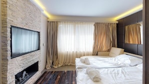 Ett hotellrum med en öppen spis i sten, en säng med vita sängkläder, en soffa och en tv som är monterad på väggen.