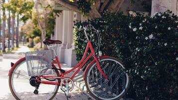 A red bicycle parked on a sidewalk next to a building with a metal fence and greenery.