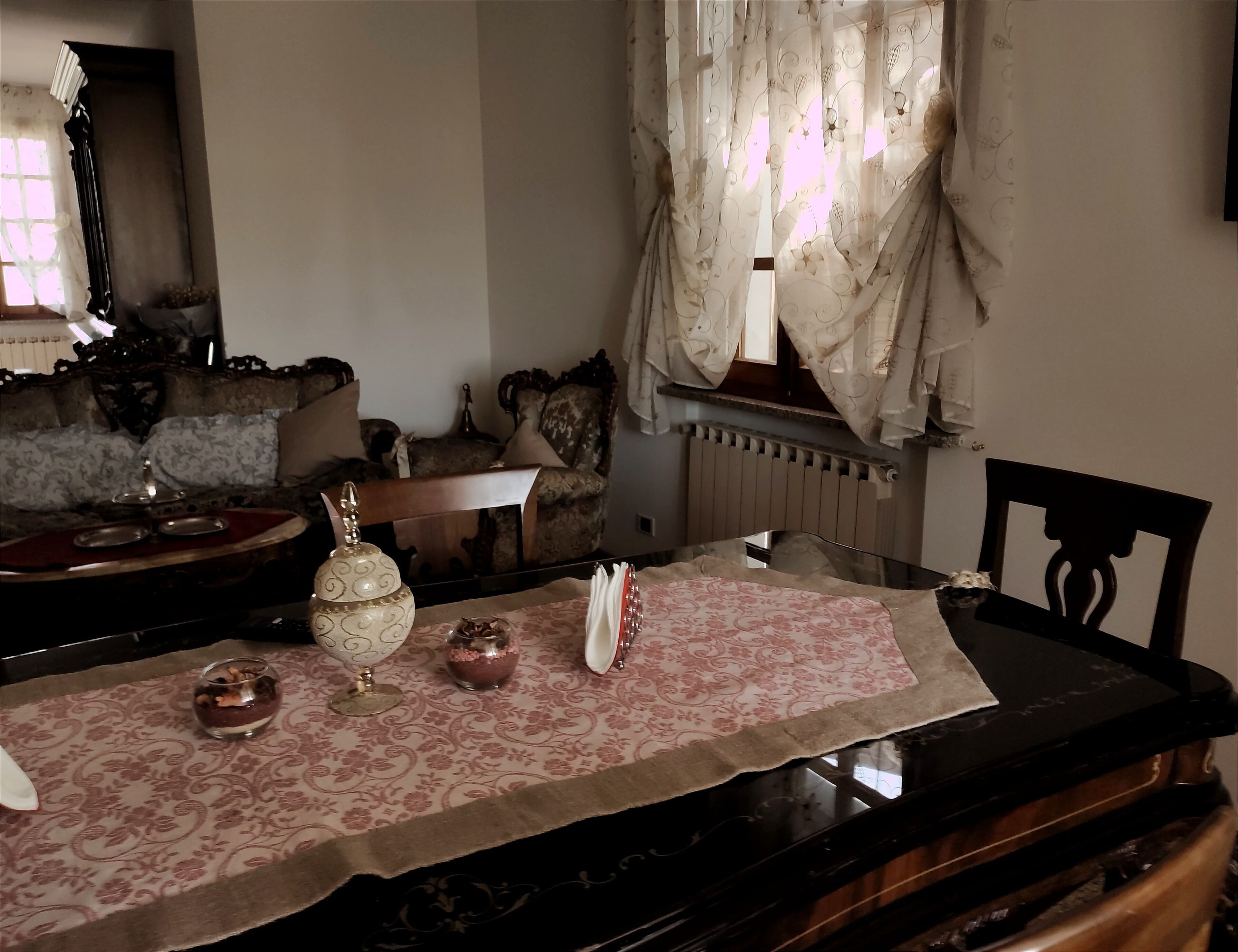 Un comedor con una mesa dispuesta para dos personas, con un mantel estampado, un jarrón decorativo y un vaso de agua.