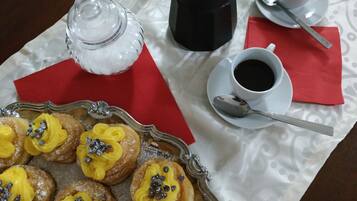 En bakke med wienerbrød, gul creme og chokoladestykker, en kaffemaskine, to kopper kaffe og en sukkerdåse på et bord.