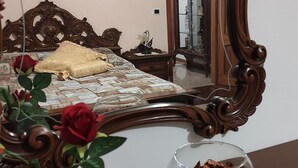 A bedroom with a large ornate mirror, a bed with a patterned bedspread, a wooden nightstand, and a vase with dried flowers. - Villa Berra B&B Riva del Po (Berra)