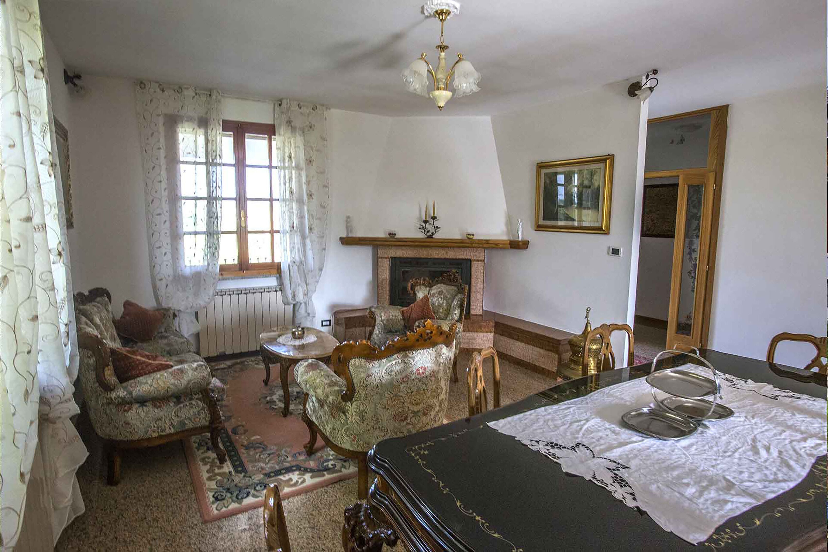 A traditional living room with a fireplace, ornate furniture, and a dining table with a lace tablecloth.