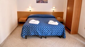 A hotel room with a checkered blue bedspread, two bedside lamps, a wooden headboard, a wooden wardrobe, and a framed picture on the wall. - Hotel Jole (Andora)