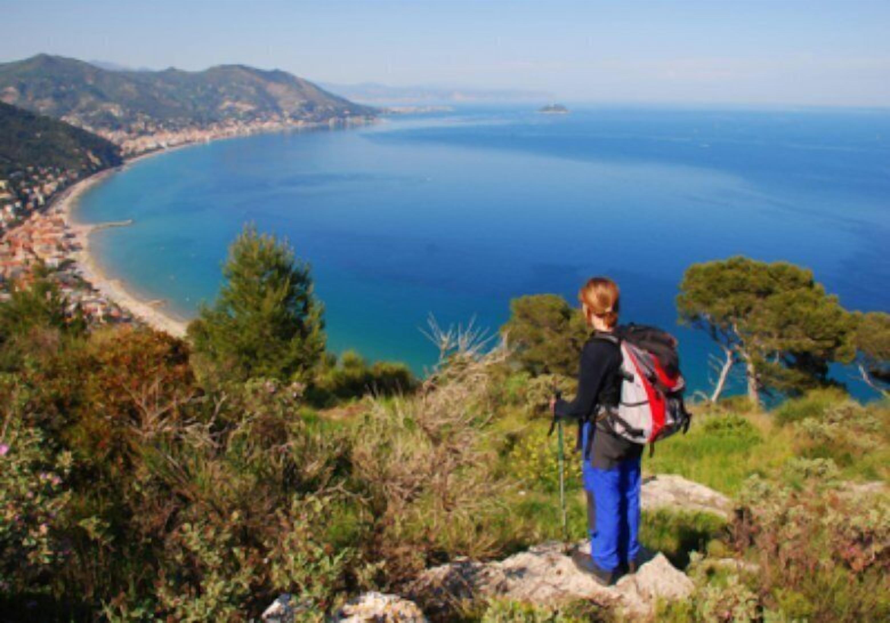 Une personne se tient sur un promontoire rocheux, d’où elle a une vue sur une ville côtière et la mer.