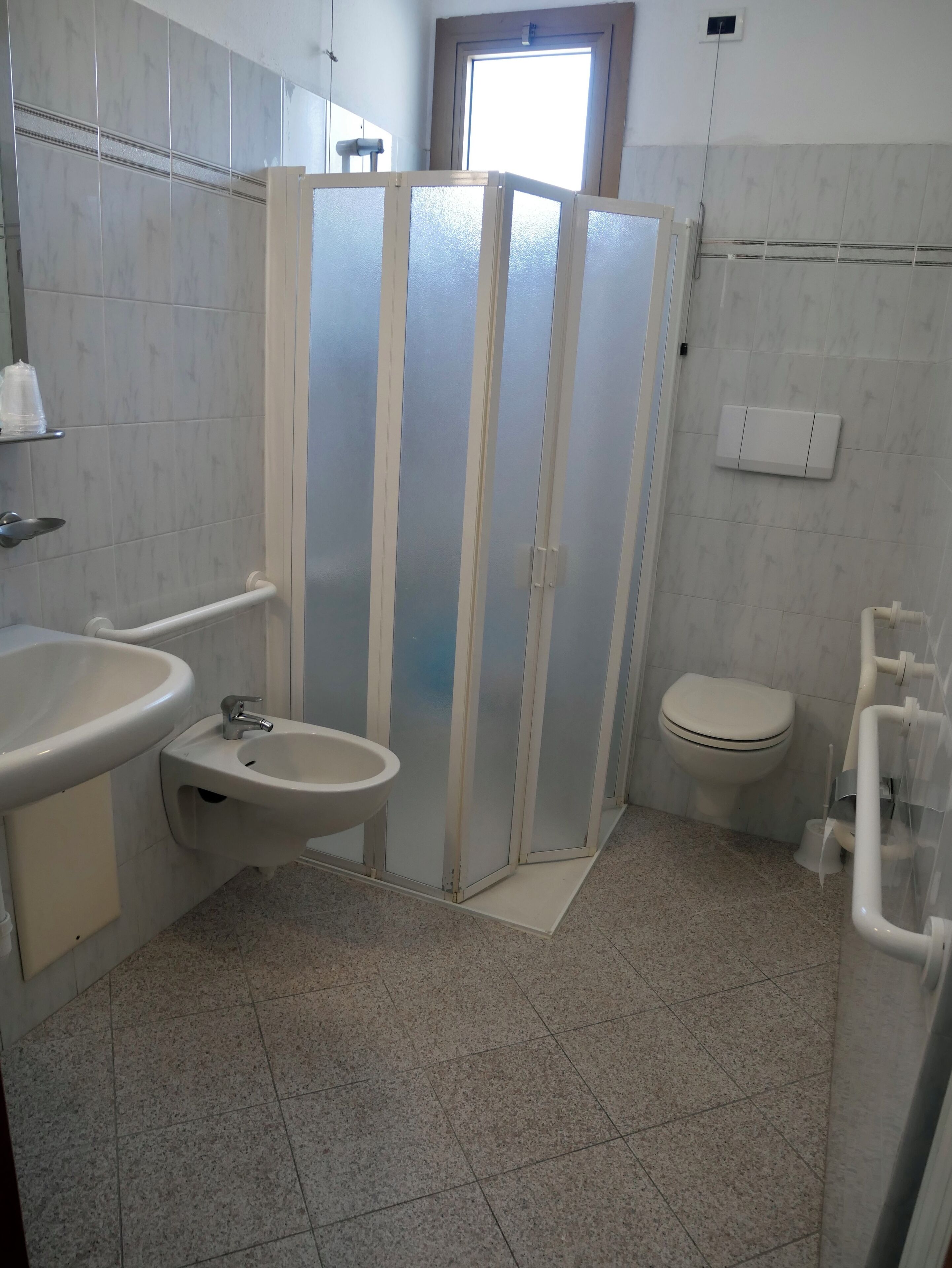 A bathroom with a sink, bidet, toilet, and frosted glass partition.