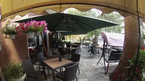 An outdoor patio area with tables and chairs under a canopy, surrounded by potted plants and flowers. - Hotel Jole (Andora)