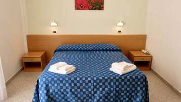 Una camera d'hotel con un letto, due comodini, una lampada a parete e un quadro con fiori rossi.