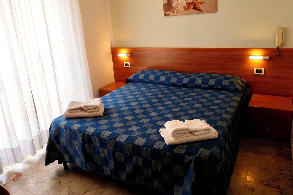 Una habitación de hotel con una colcha a cuadros, dos lámparas de noche, un cuadro en la pared y un cabecero de madera.