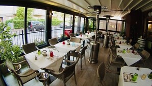 A restaurant with tables and chairs, large windows, and a view of the street. - Hotel Jole (Andora)