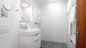 A modern bathroom with a white sink, mirror, and shower. - Popular and centrally located residential building in St. (St. Moritz)