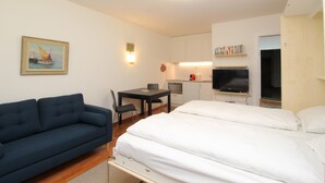 A hotel room with a bed, a sofa, a desk with a chair, a TV, and a small kitchenette. - Popular and centrally located residential building in St. (St. Moritz)