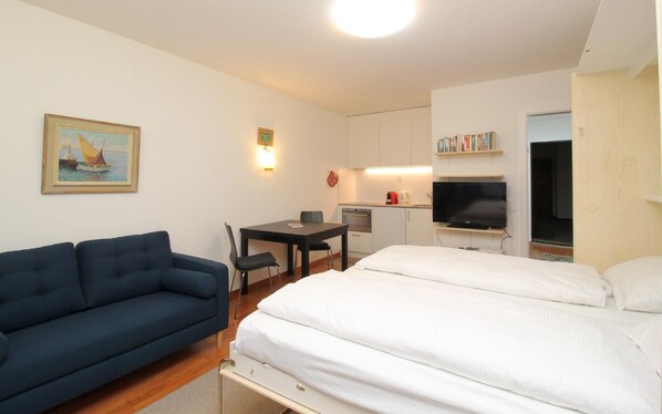 Quarto de hotel com uma cama, um sofá, uma secretária com cadeira, televisão e uma pequena copa.