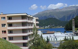 En byggnad med flera våningar, balkonger och utsikt över en sjö, med berg i bakgrunden.